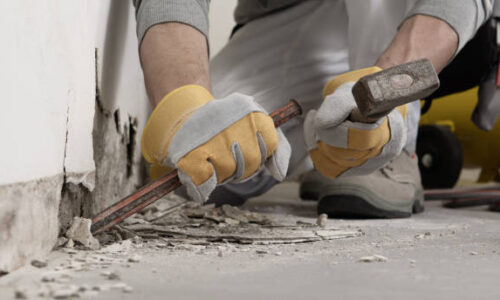 Interior demolition: Construction worker hands with gloves working with hammer and chisel to remove old plaster from wall for house renovation, close up with rubble