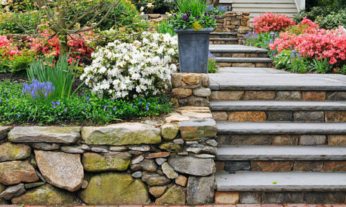 Stone wall, steps and planter on colorful, landscaped garden.