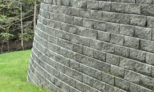 tall stone retaining wall (curved brick masonry) in house back yard (large gray supporting structure)